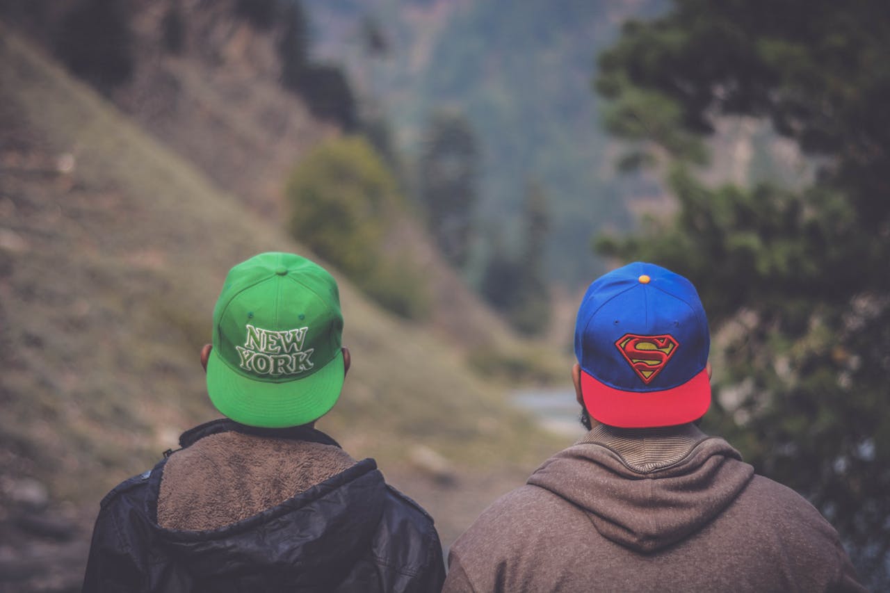 gallery-1 Back view of two friends wearing caps in a scenic outdoor landscape setting.