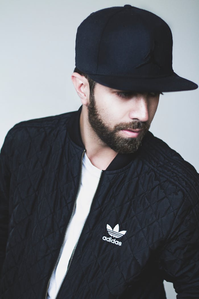 gallery-4 Portrait of a man in a black Adidas jacket and cap, looking down.