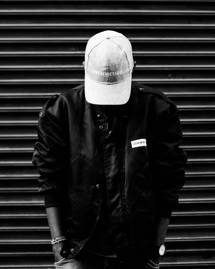 services-03 Black and white portrait of a person wearing a cap and jacket, posing confidently.