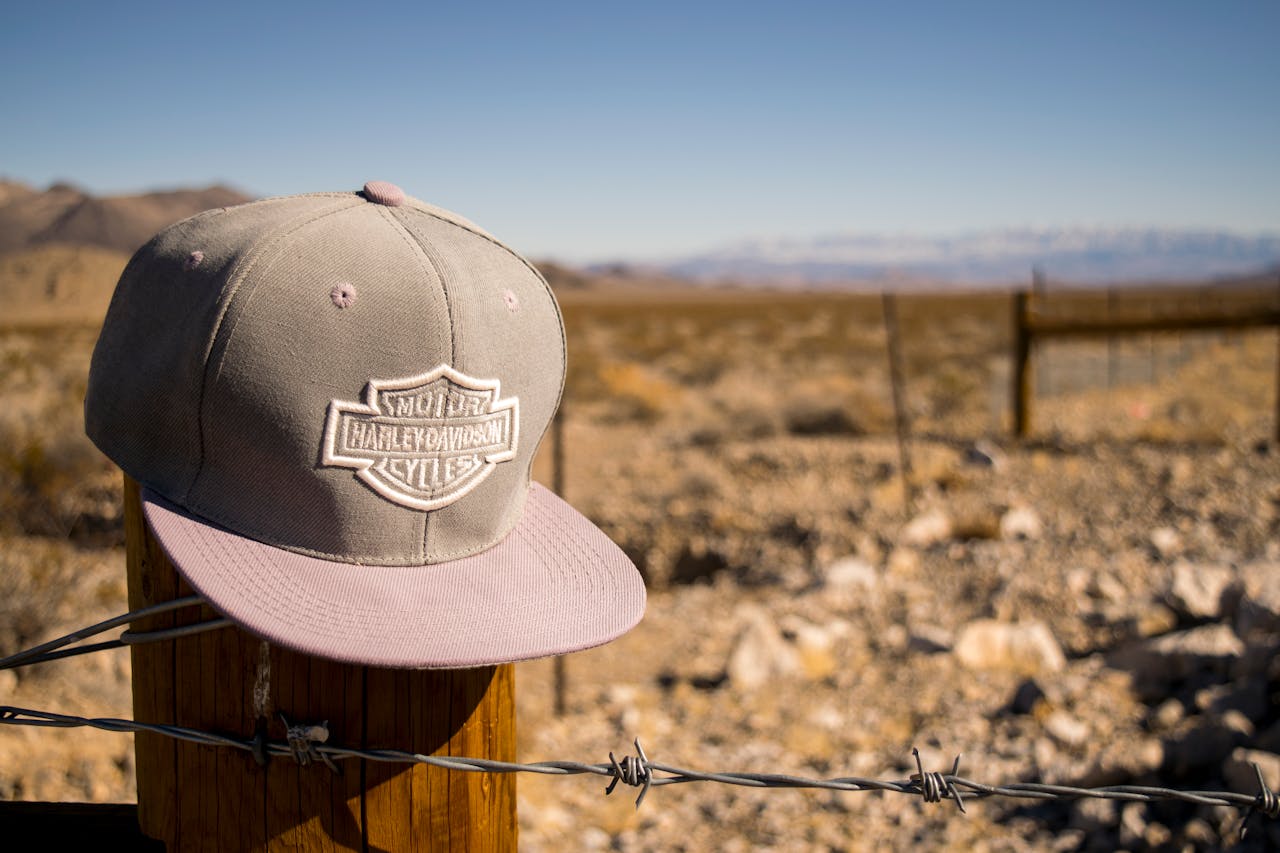our-services-2 A Harley Davidson cap sits on a fence post in an arid desert landscape, under a bright blue sky.